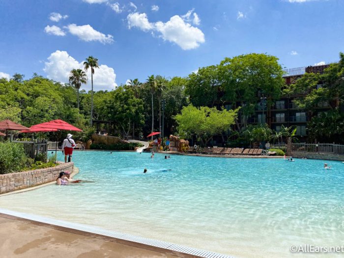 Image shows a blue swimming pool in a hotel grounds
