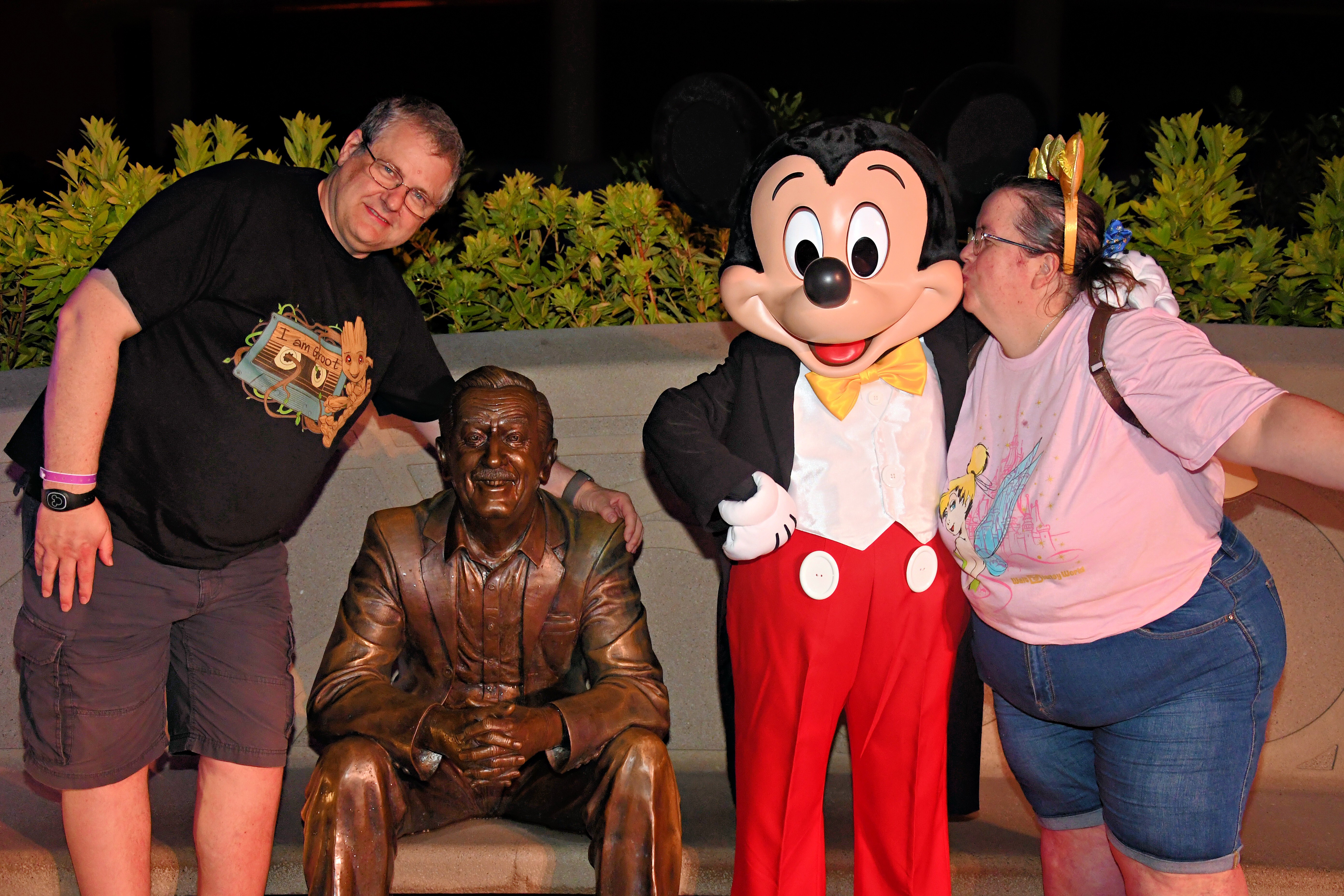 mickey mouse standing with a man and woman next to a bronze statue