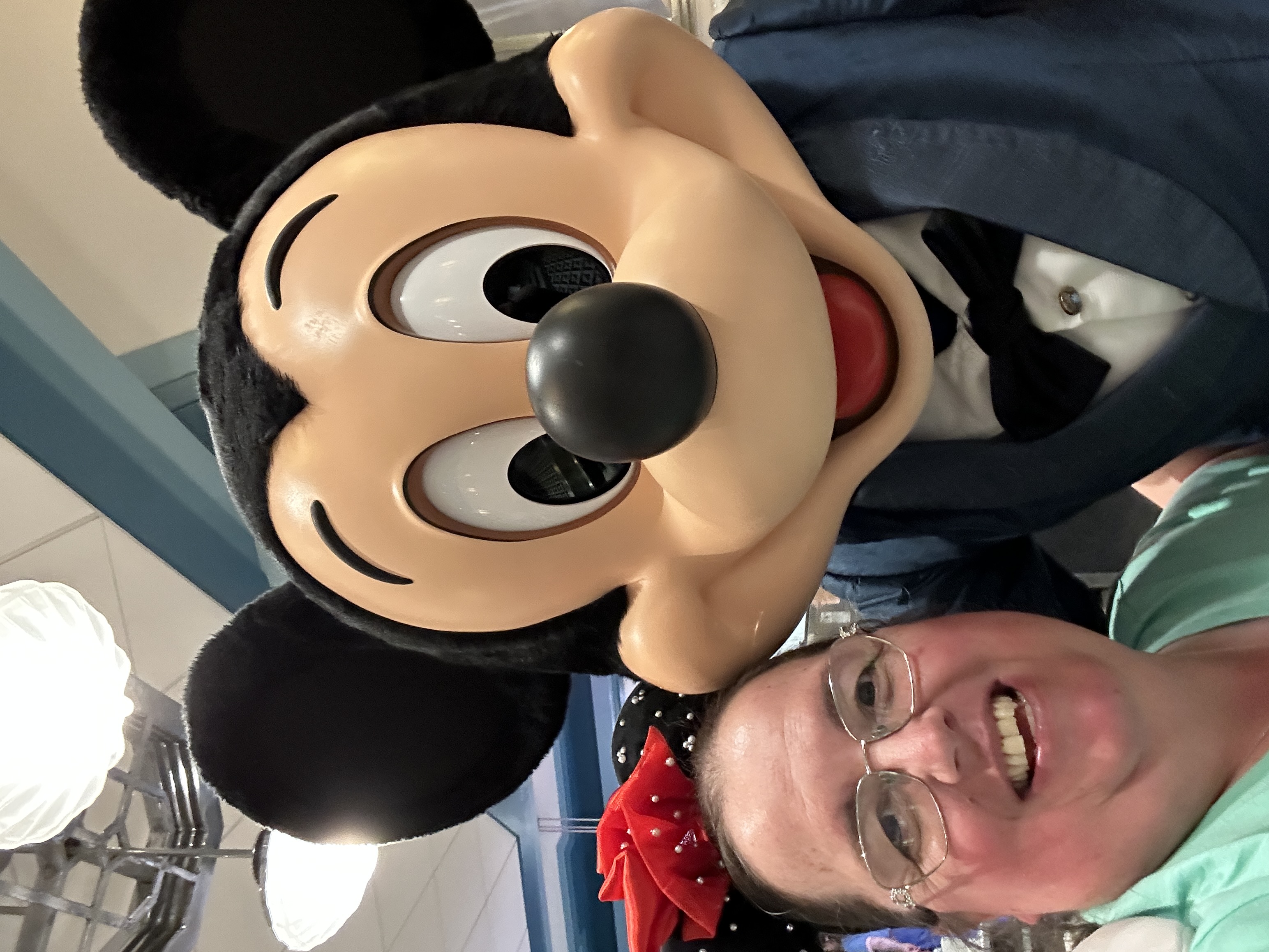 Image is a lady smiling with Mickey Mouse standing next to her