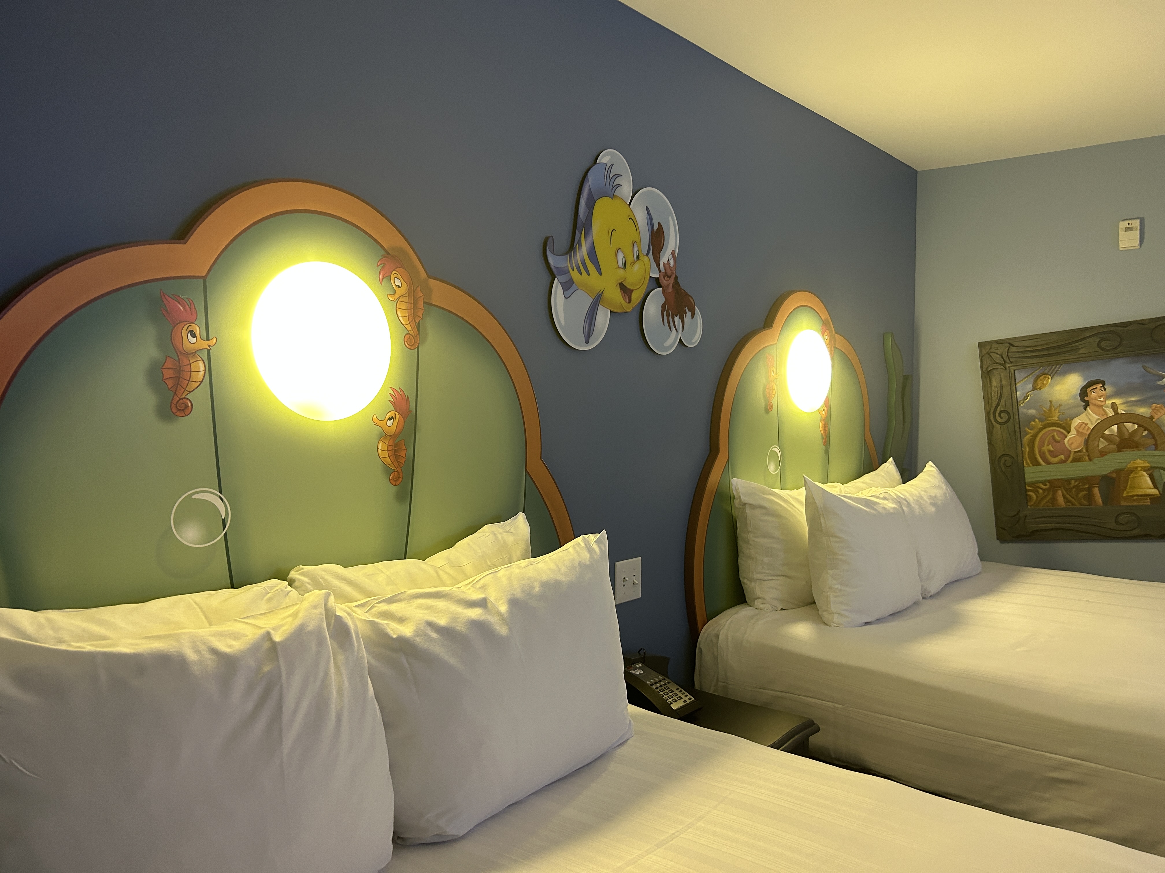 Image shows a bedroom with two large double beds and a blue and yellow fish on the wall