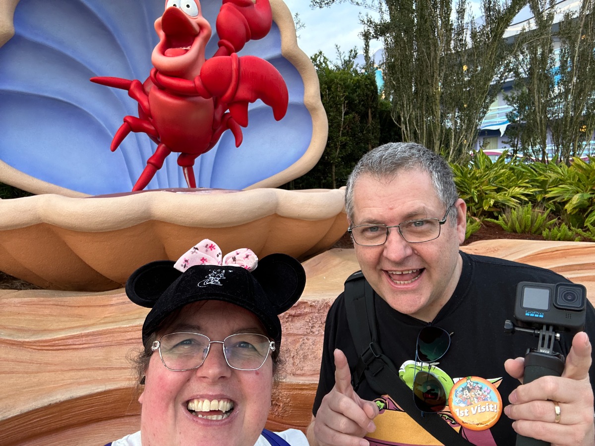 Image shows a man and a woman standing in front of a shell with a red lobster disney character inside