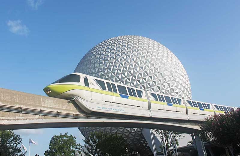 Image shows a train style transport on a raised rail passing infront of spaceship earth which looks like a golf ball