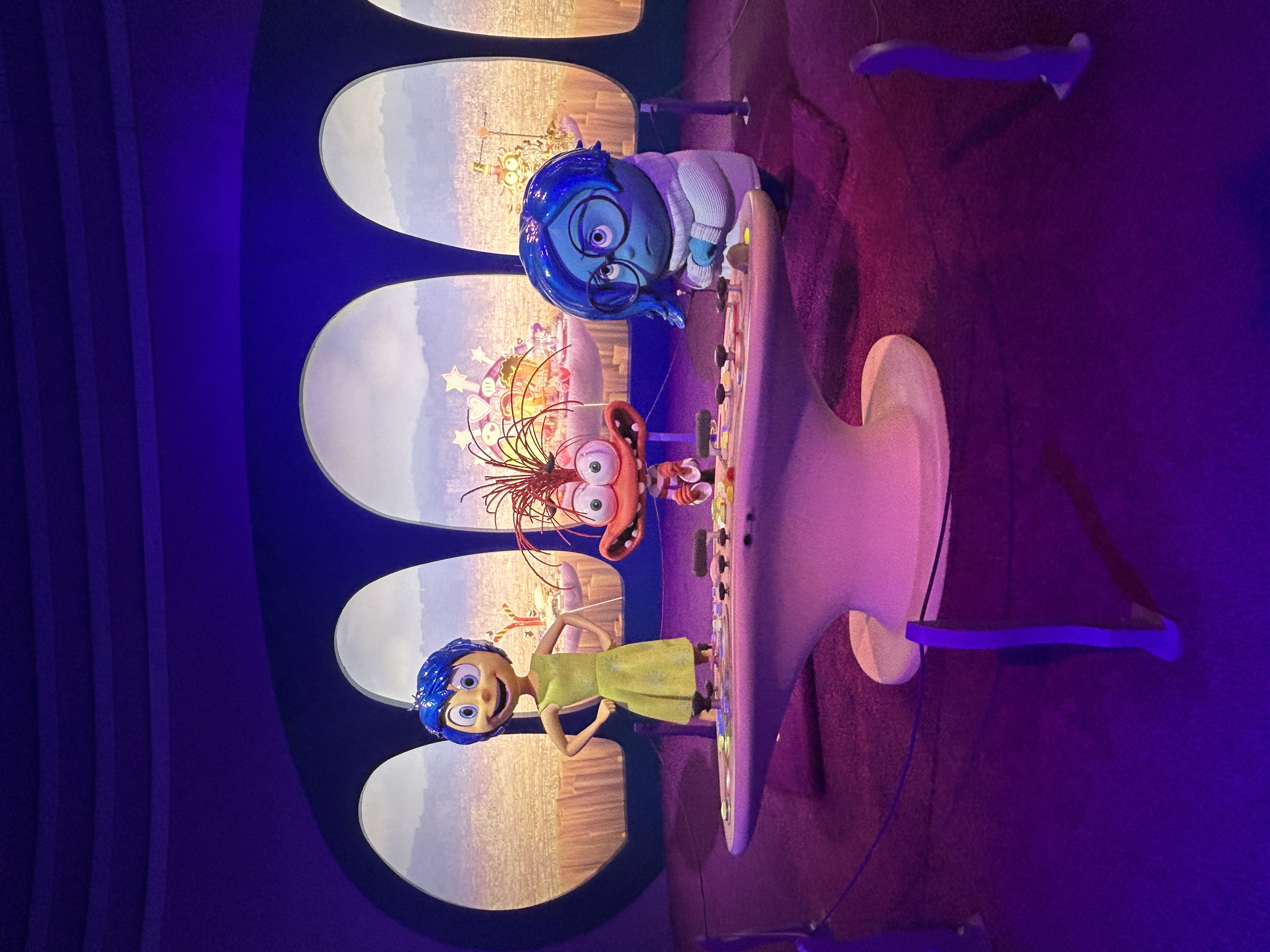 A room with oval windows, three characters, and a control desk covered in buttons