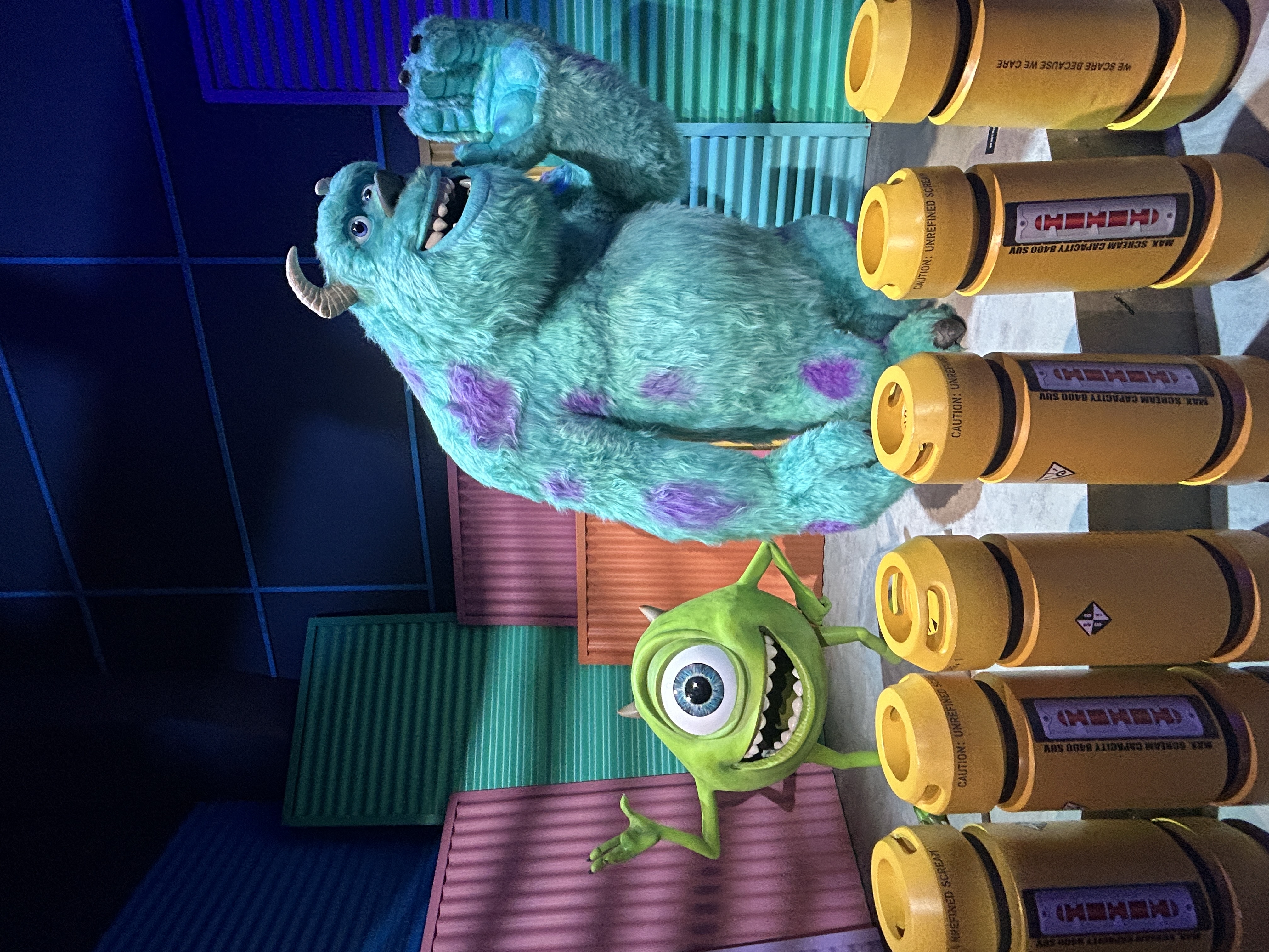 A round green one-eyed monster and a blue fluffy monster with purple spots, surrounded by yellow canisters