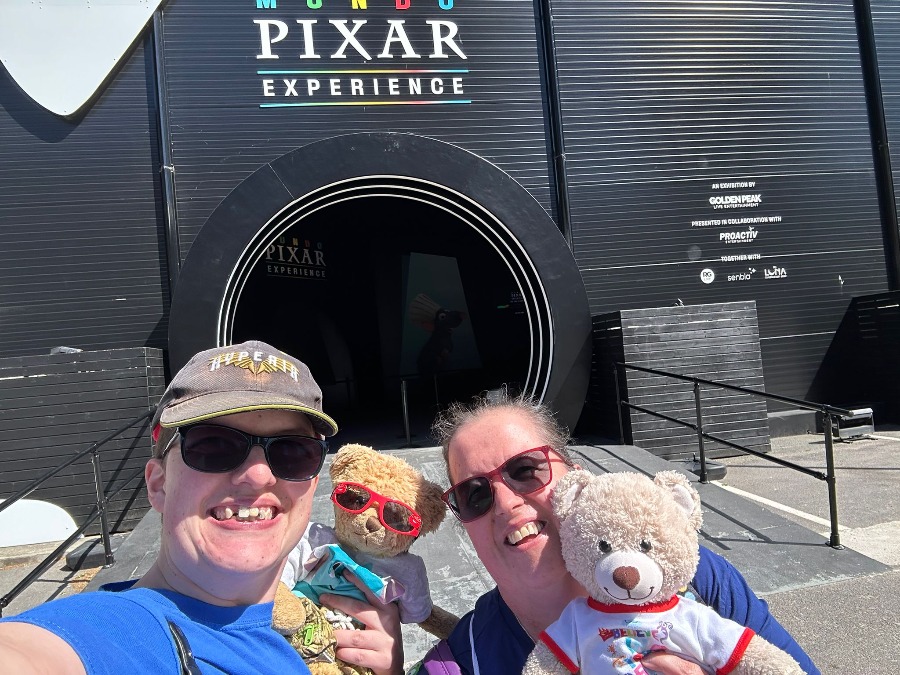 Pictures shows a black building with the words Mundo Pixar on , with a Woman in sunglases holder a teddy bear in front of