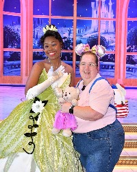 Image shows a lady wearing mickey mouse headband standing next to Tiana a disney princess