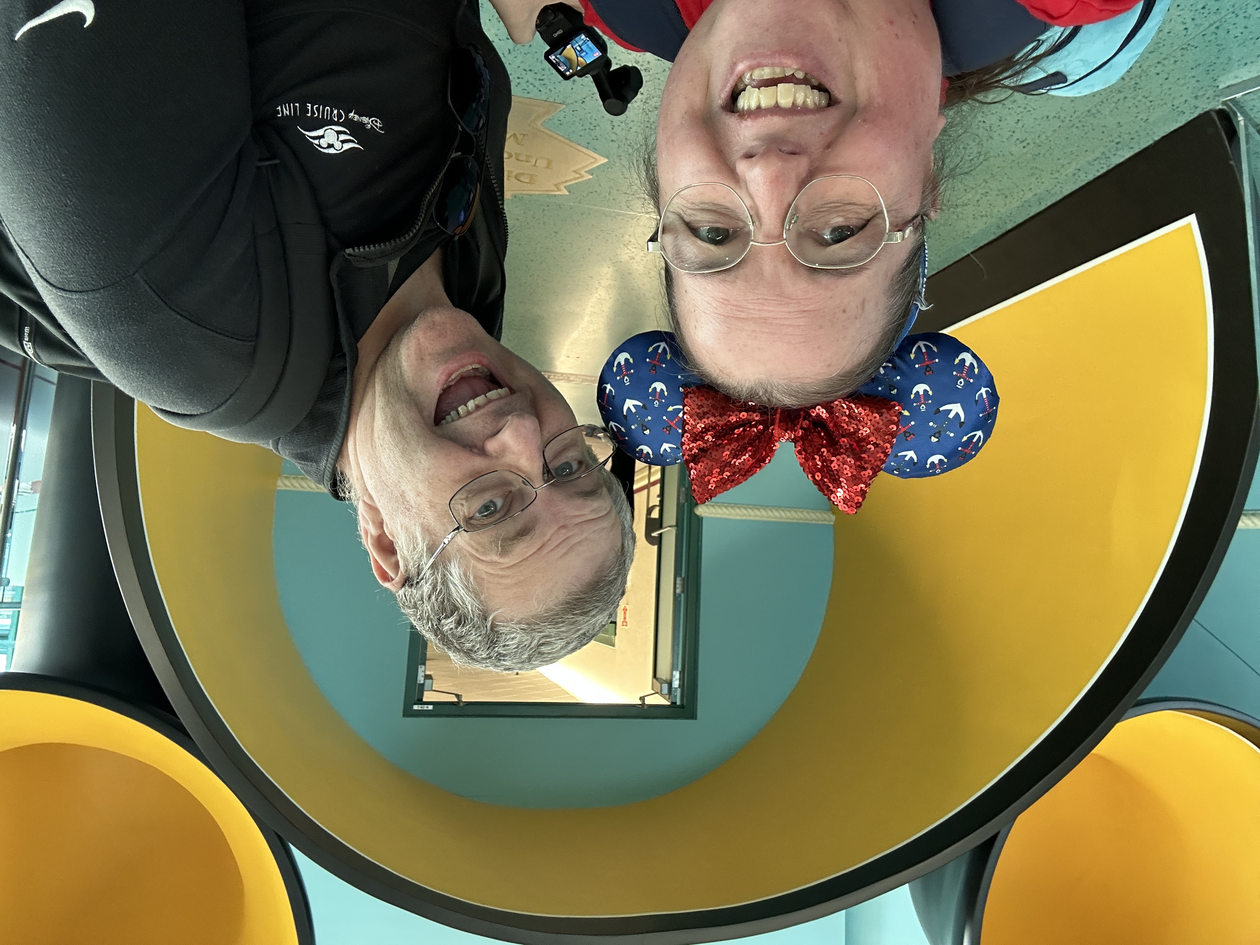 Two adults standing in front of a yellow mouse shaped archway smiling