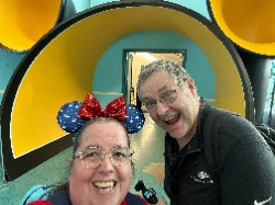Image show a man and Lady in front of a Mickey Head archway