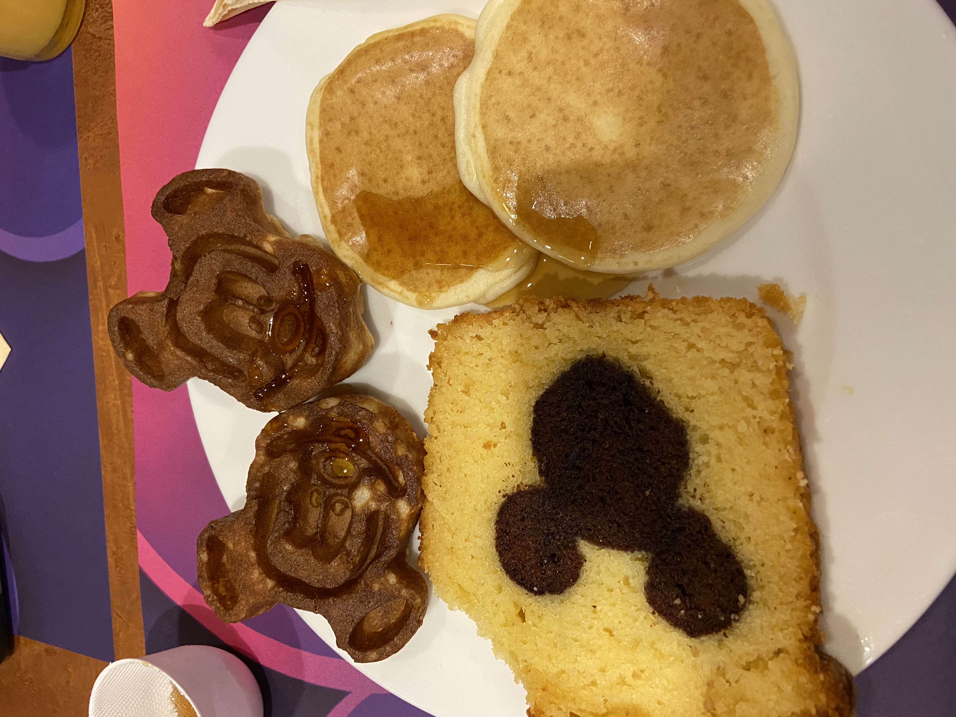 A plate with two Mickey-shaped waffles, two pancakes and a slice of cake